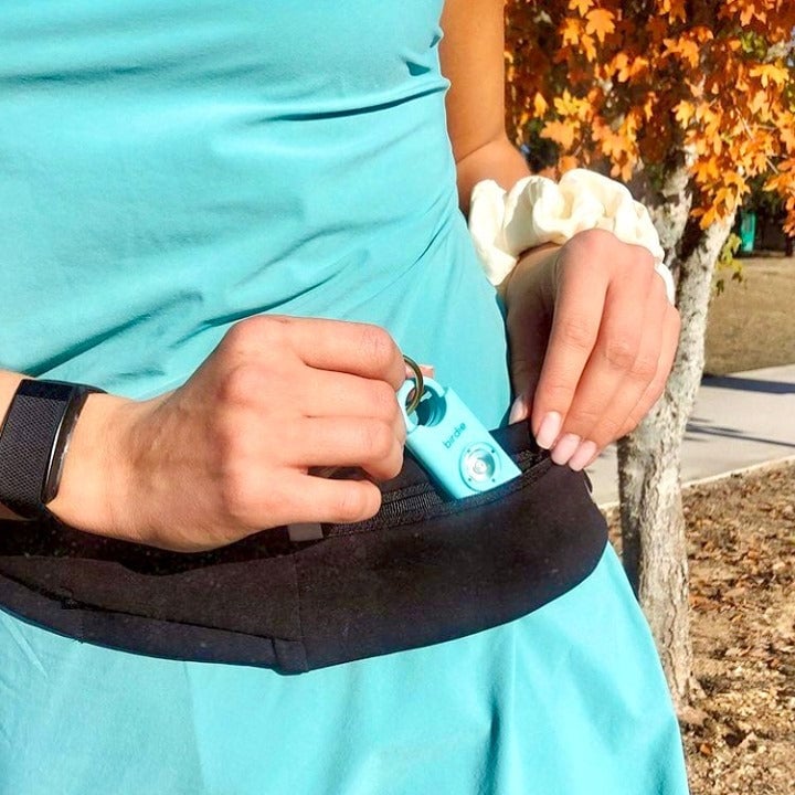Person clipping a blue portable device onto a black waistband.