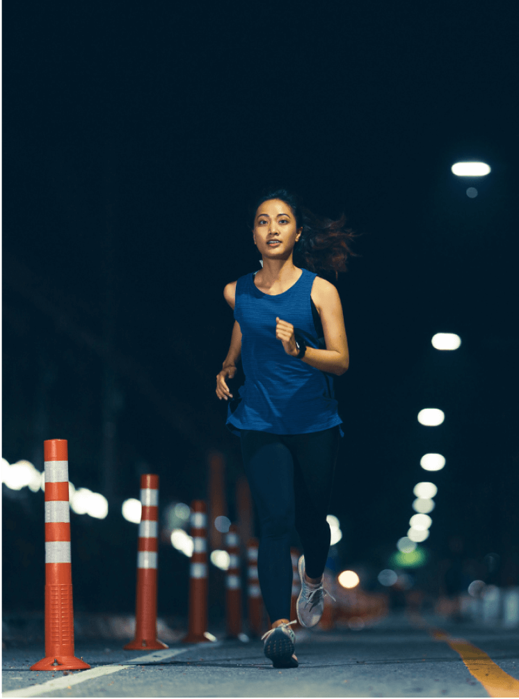 Woman running at night on a road lined with orange cones.