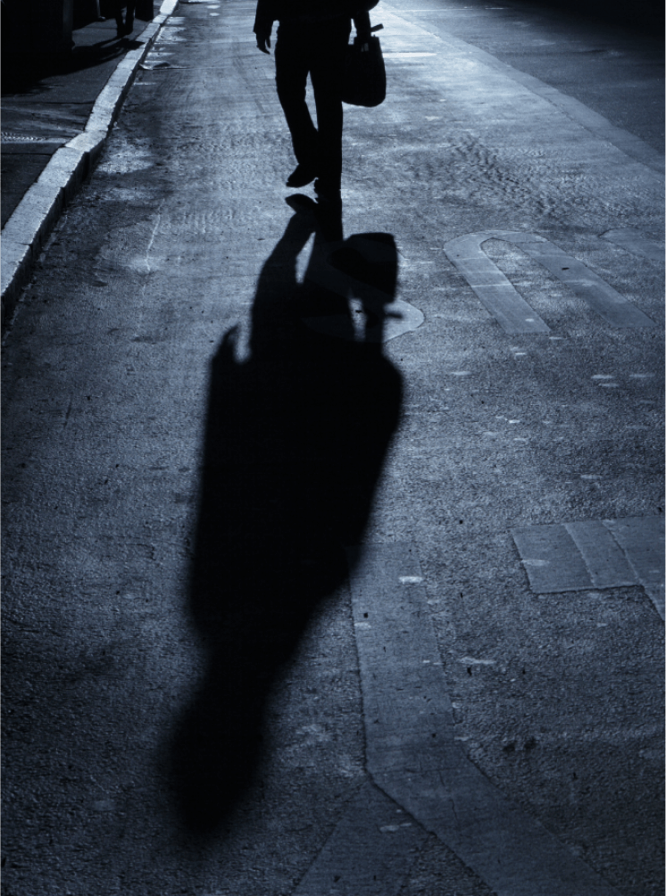 Silhouette of a person walking on a dimly lit street at night, casting a long shadow.