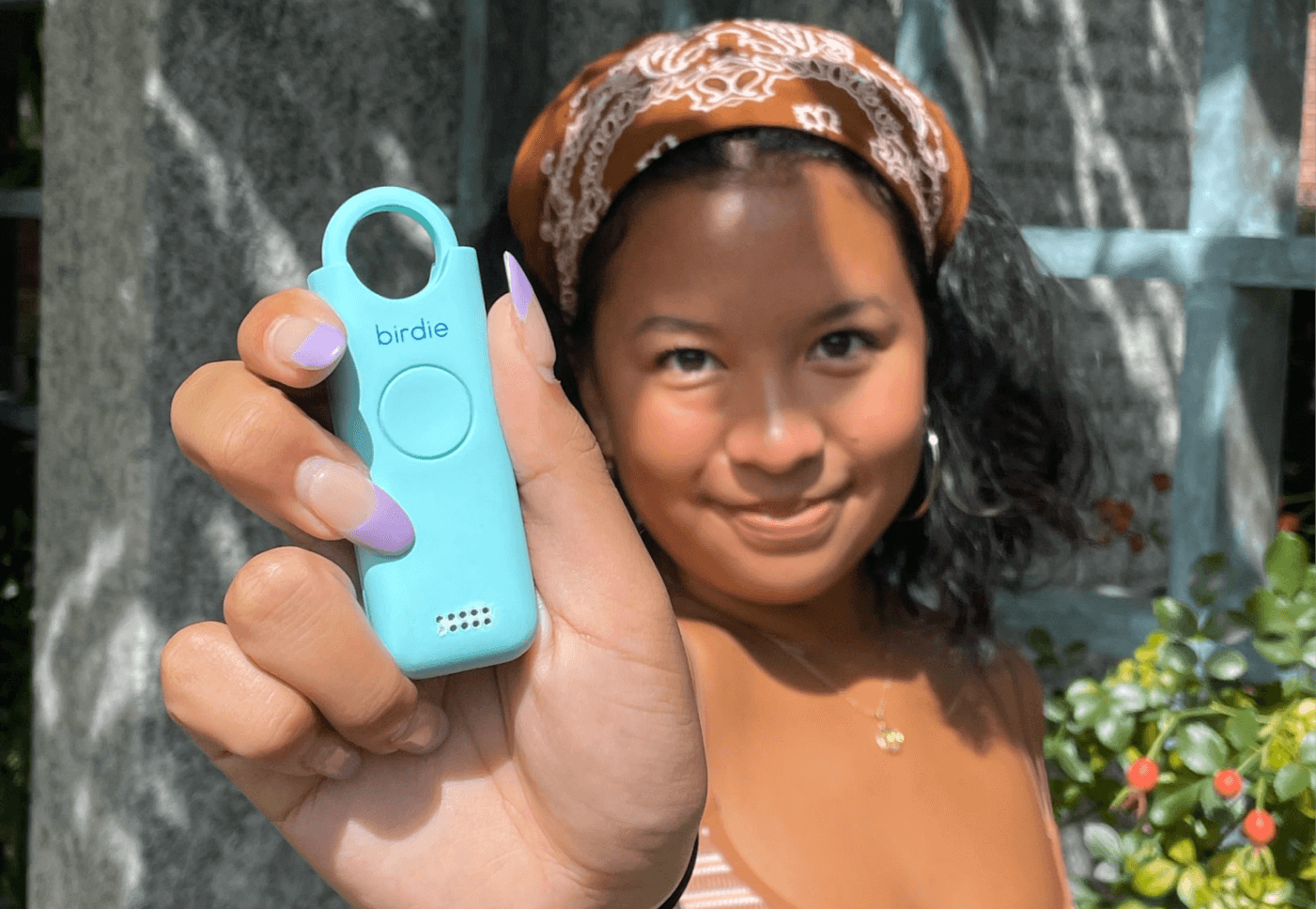 A smiling person holding a blue personal safety alarm device called 'birdie.'