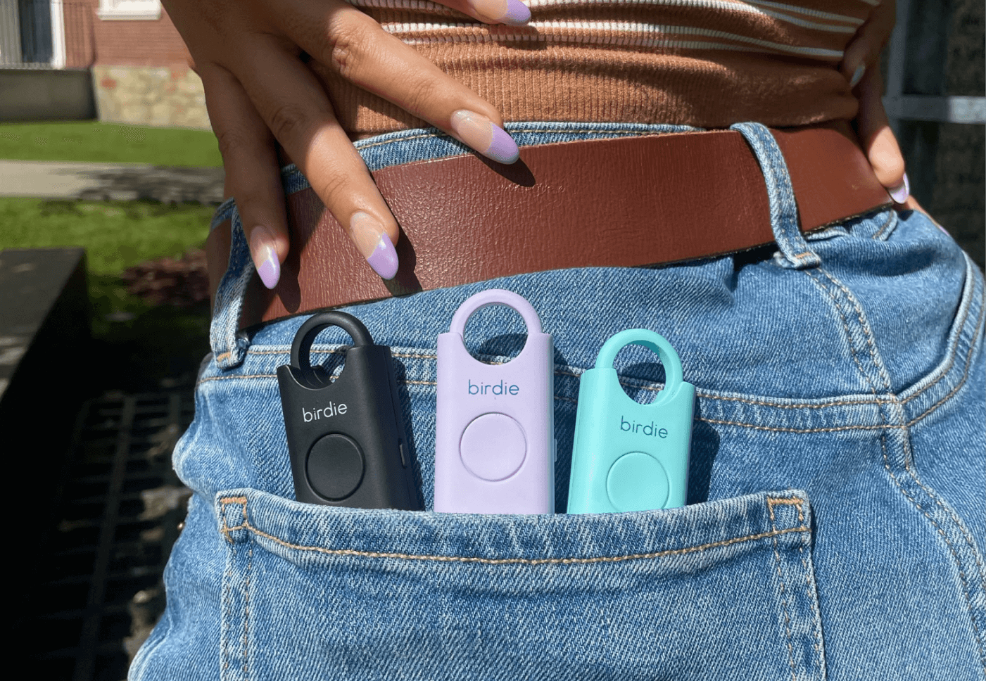 Person with colorful nails holding a waist bag with three personal safety alarms attached.