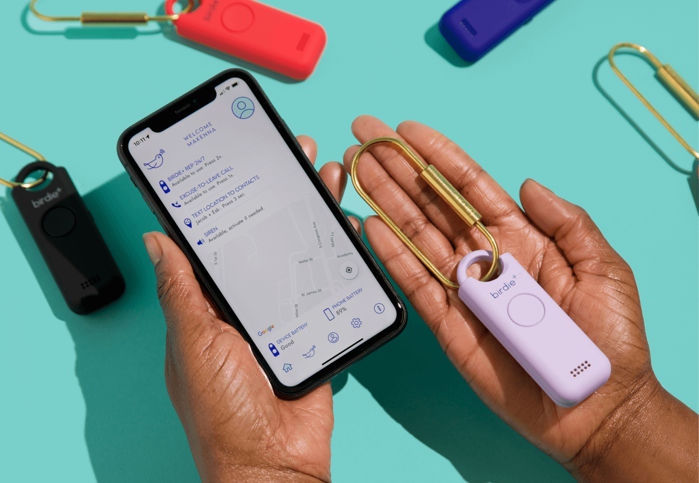 Hand holding a smartphone and a personal safety device with other colorful devices in the background.