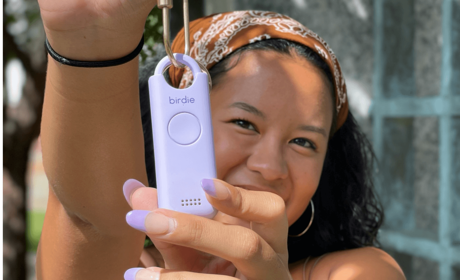 A person holding a personal safety alarm named 'birdie' and smiling at the camera.