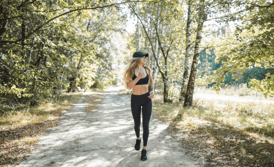 Woman jogging on a forest trail path in athletic wear and cap.