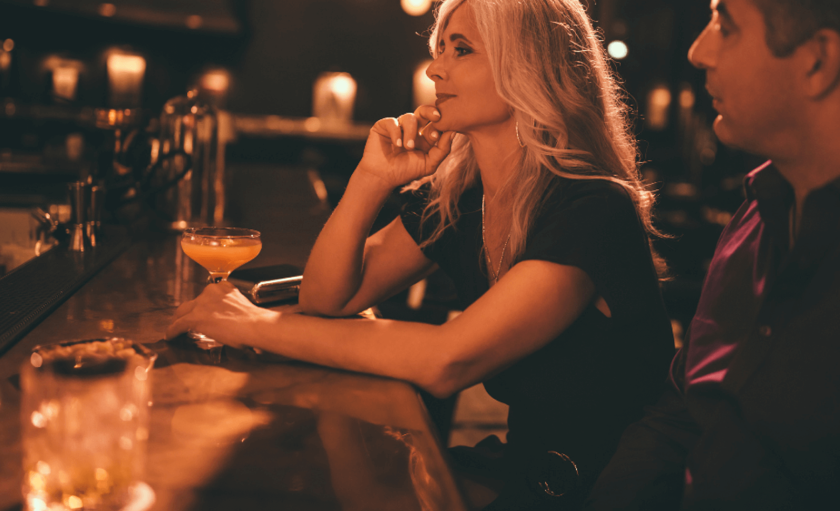 Woman sitting at bar beside a man, contemplating, with drinks on the counter.