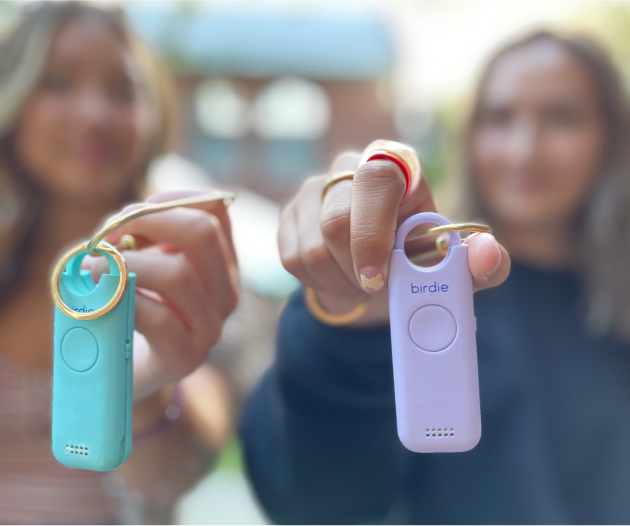 Two people holding personal safety alarms on keychains, shown in focus against a blurred background.