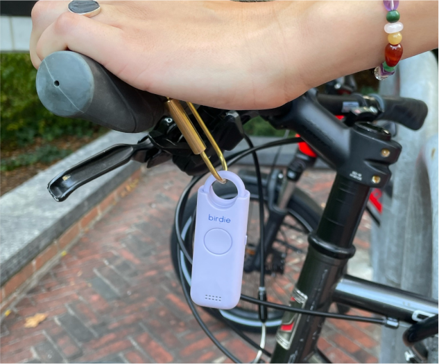 A hand holding a personal safety alarm attached to bicycle handlebars.