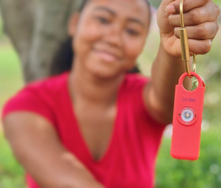 Person holding a red personal safety alarm outdoors.