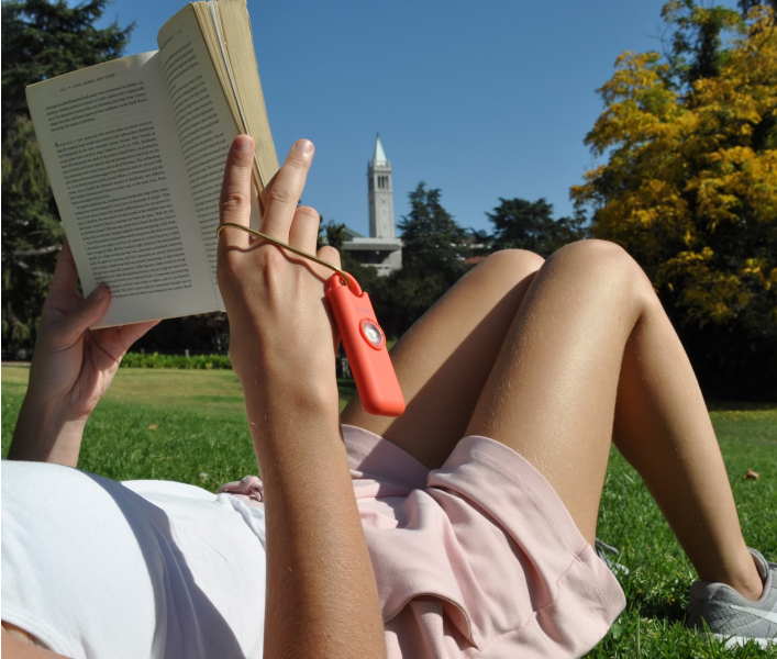 Person reading a book on the grass, wearing a page holder on a sunny day.