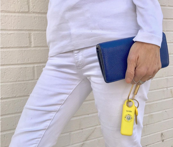 Person holding a blue wallet and yellow keychain against a white brick wall.