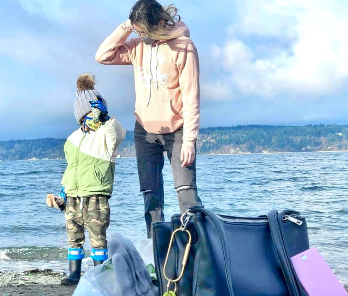Person and child on beach by water, with bag and gloves in foreground.
