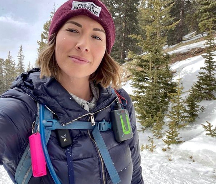 Person hiking in snowy forest wearing winter gear and a maroon beanie.